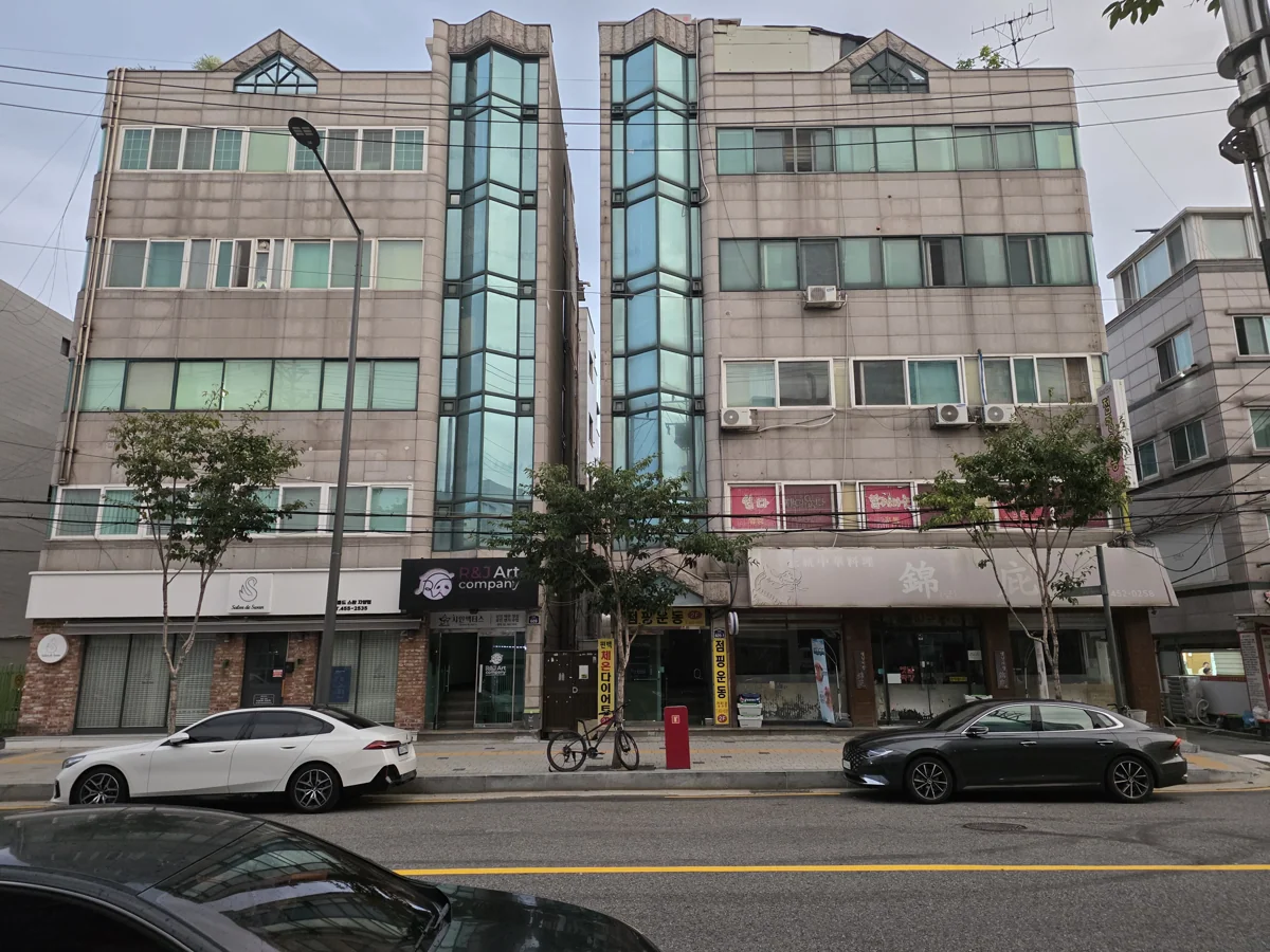 청록색 유리 계단탑과 상점들이 보이는 뚝섬로 거리